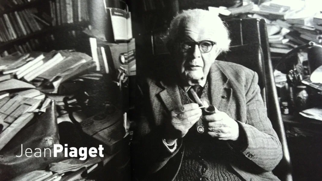 Foto em preto e branco de Jean Piaget sentado em sua mesa, trabalhando em suas teorias sobre a construção do conhecimento e a educação.