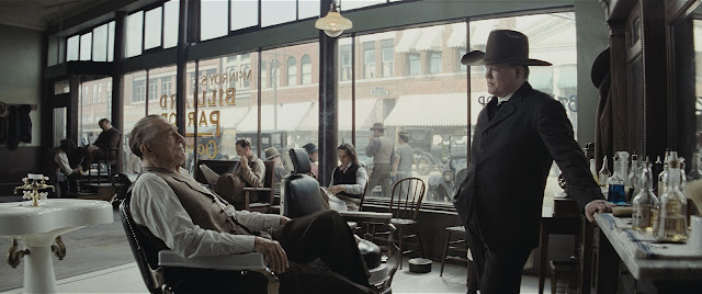 A man in a cowboy hat questions a man sitting in barber's chair