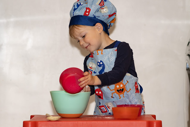 a preschooler standing behind a table mixing cake ingredients together