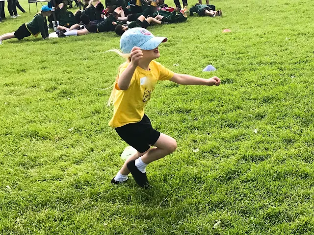 A young girl is running a race in school sports day, her hat is pulled so far down on her head she can hardly see where she is going.