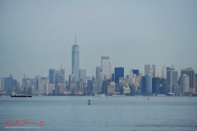 A hazy view of the Manhattan skyline and shipping buoys photographed from the Staten Island Ferry on Manhattan Harbor.  Travel photography by Kent Johnson.