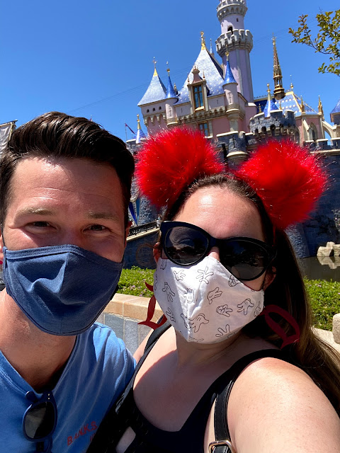 Friends wearing masks and smiling in front of Sleeping Beauty Castle at Disneyland.