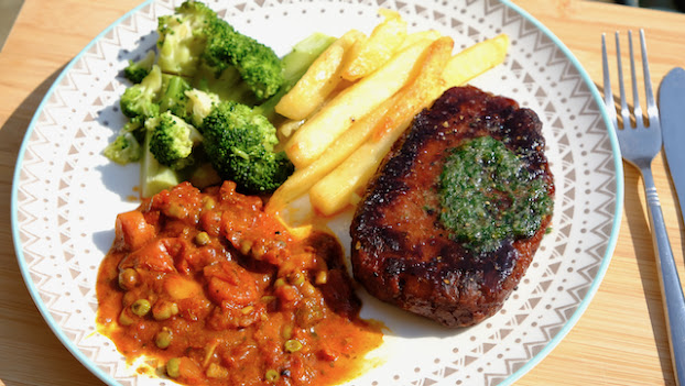 Vegan steak on a plate with chips, veg and tomato sauce