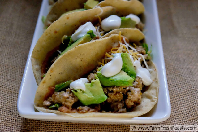 image of corn tortillas with refried beans, salsa verde pork, avocado and sour cream