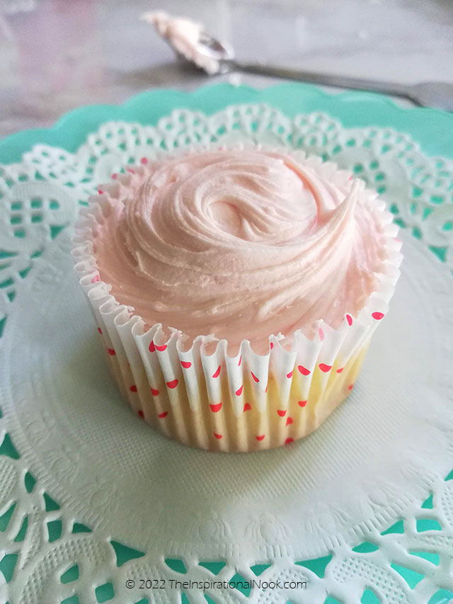 Pretty pink cupcake with cream chees frosting on a turquoise plate and paper doily