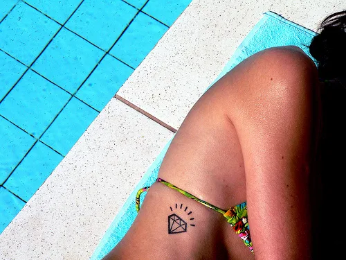 chica en una piscina, esta en bikini, vemos en su costado un tatuaje de diamante