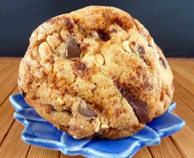 Chocolate Chip Cookie made with browned butter, chopped chocolate, peanuts, and caramel, pictured on a blue flower-shaped plate