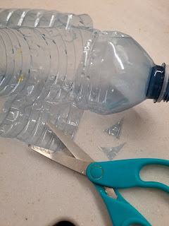 Empty 500ml water bottle with cuts made for two wings . A pair of scissors and plastic snipped from the wings lay beside it on the counter.