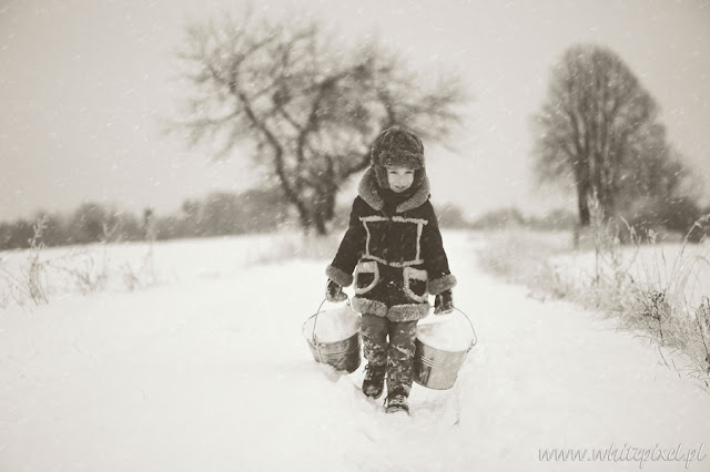 Mały szczęśliwy chłopiec pozuje do fotografi na sesji zdjęciowej w zimowym plenerze