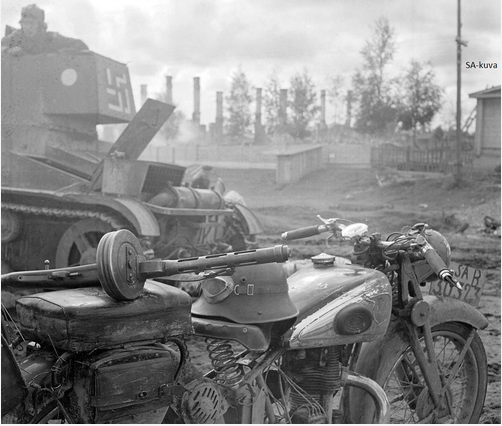 Finnish motorcycle couriers bike and his Suomi submachine-gun M-31 and on the background T-26 where its commander is out of the hatch. Somewhere in the eastern front 1941-1944.PNG