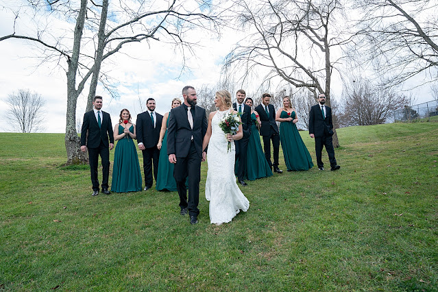 bride and Groom holding hands and looking at each other as they walk forward with bridal party looking from behind Magnolia Farm Asheville Wedding Photography captured by Houghton Photography