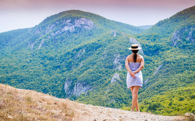 Back of woman wearing hat and skirt looks at mountain