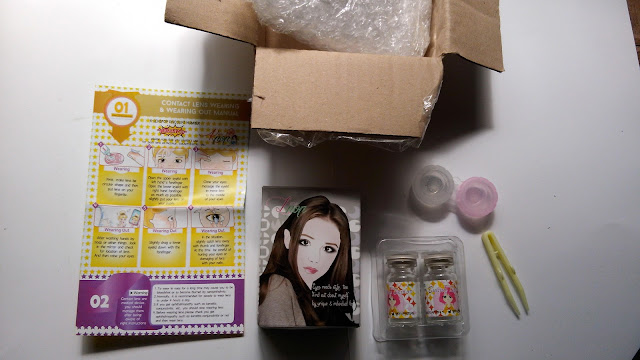 Inside the brown box is the package. The pack (with picture of a pretty brown haired girl) is carefully covered in a bubble wrap so it is very safe and protected against rough handling and the far travel. It contains a plastic lens case, a manual, plastic tweezers to handle the lens and 2 glass bottles containing the lens itself.