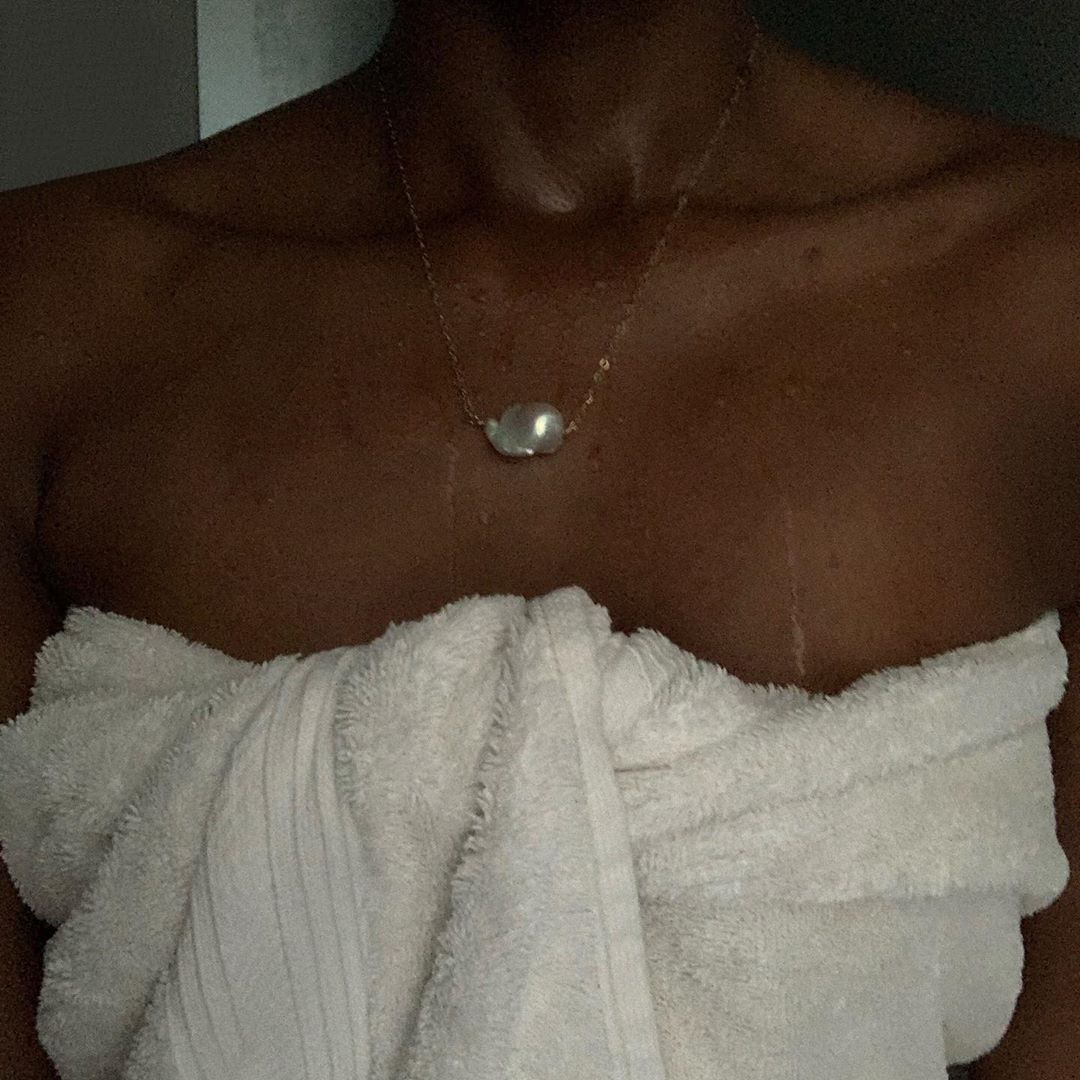 Woman wrapped in a towel wearing a gold chain with a large baroque pearl pendant