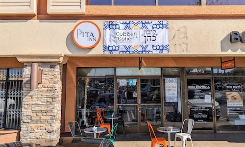 Restaurant facade in plaza, only a banner sign has been hung so far and the old Pita Inn sign is visible.