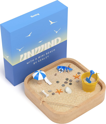 A small desk size, sand garden with brown sand and a set of figurines with a beach theme, a beach chair, a yellow sand bucket, a little two person wooden fishing boat, shells, and a sand rake. Fun, decorative, therapeutic, magical.