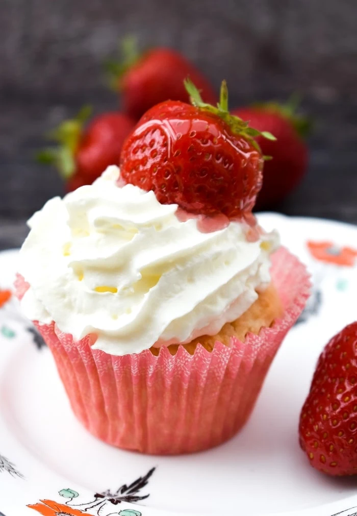 close up of a vanilla muffin topped with whipped cream and a glazed strawberry