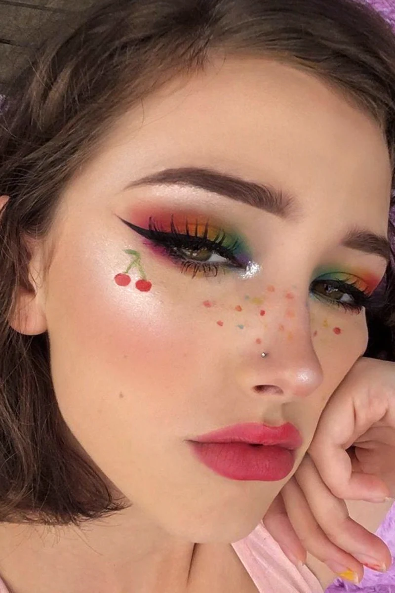 a close-up selfie of a young beautiful e-girl with rainbow makeup look and cherry drawing on her cheek