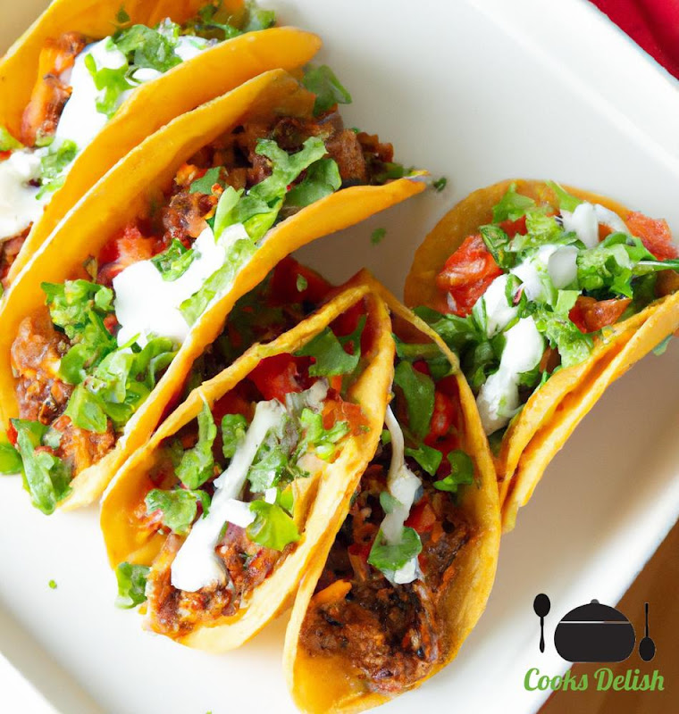 Image of beef tacos with a variety of toppings including lettuce, tomato, cheese, and sour cream. The beef is seasoned with a blend of spices and is cooked to perfection. The tacos are served on warm tortillas and are garnished with fresh cilantro.