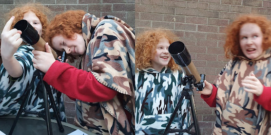 Boys messing about and making each other laugh  with telescope in garden