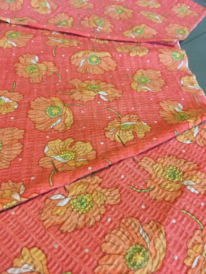 A close-up of three panels of bright coral fabric with orange poppy flower print, pinned to fniishe the seams between panels.