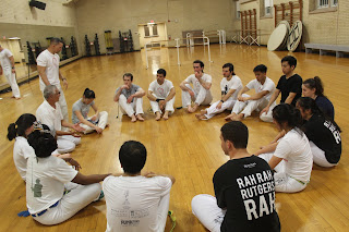 A group of students sit in a circle, listening the wisdom of a capoeira master.