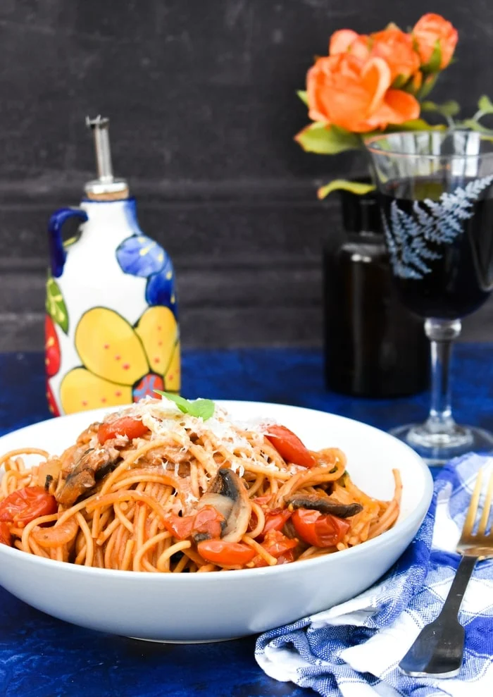 A bowl of spaghetti on a table with wine and flowers