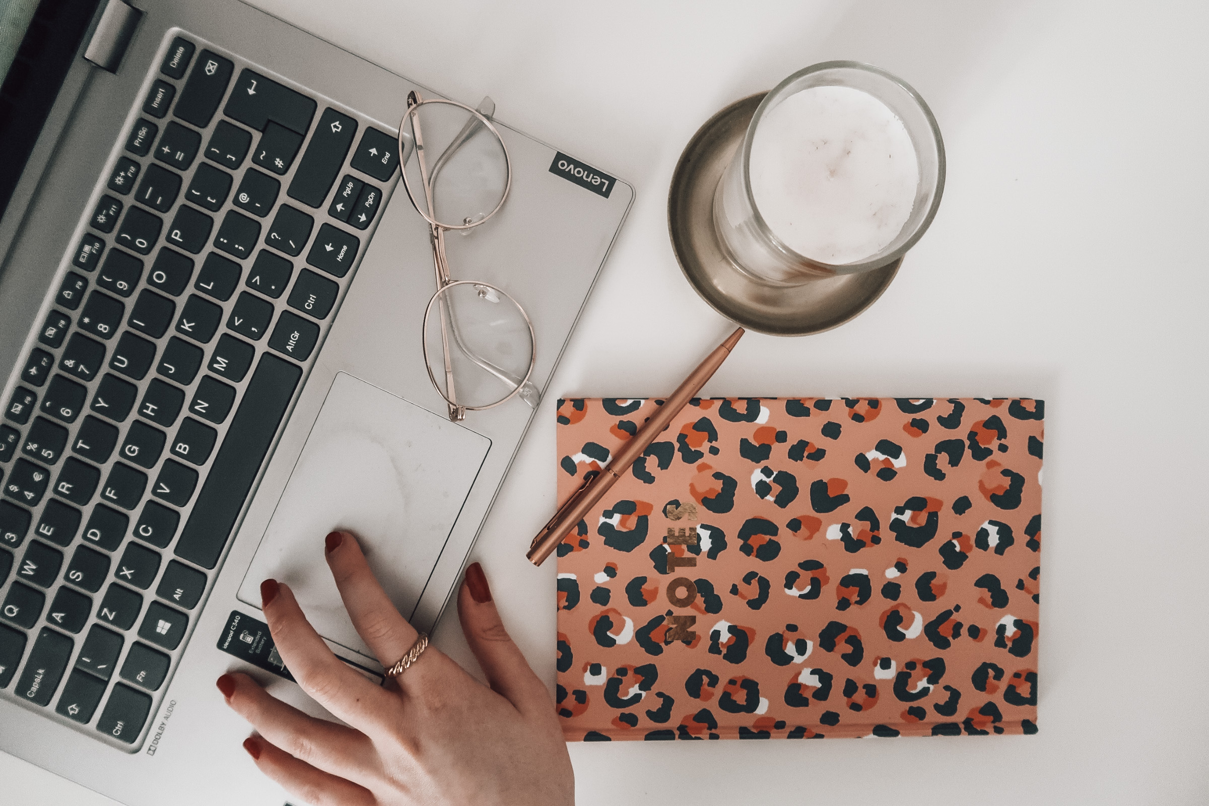 A laptop, a candle, a pair of gold-framed glasses and a pink leopard print notebook.