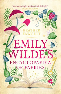 Cover for book "Emily Wilde's Encylopedia of Faeries" by Heather Fawcett. At the bottom, an open book. Above, a rambling border of drawings of farms, mushrooms, berries, ivy and stars. A golden key is wrapped around with twining tendrils.