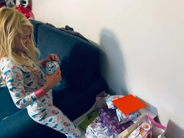 An 8 year old girl with long hair and mermaid pyjamas opening presents on her 8th birthday