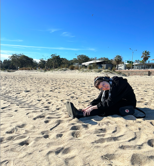 Sunny day at the beach. I'm in the middle of the photo, trying to reach my feet, wearing black winter clothes and looking at you.