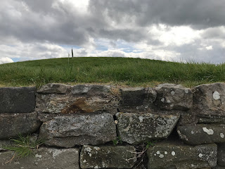 A photo of a small, ceramic skull (Skulferatu 72) sitting in a gap in the wall that is around Huly Hill Cairn.   Photo by Kevin Nosferatu for the Skulferatu Project.