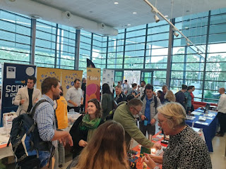 Bright conference registration foyer with mingling attendees browsing information tables.