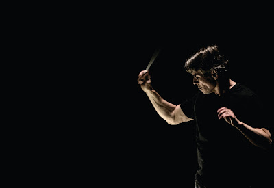 Esa-Pekka Salonen, conducting, in profile, in a black t-shirt against a black background