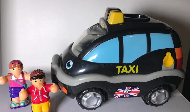 A toy black taxi and 2 tourist looking figures