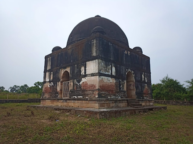 Discoloured domed square tomb structure in grassy area in Champaner