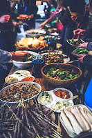 A buffet table with a range of food upon it. People are serving themselves from the table.