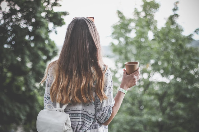 light haired woman's back facing us holding a latte looking drink in right hand