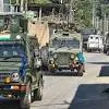 Military convoy with armed vehicles and troops moving through a city street, other civilian vehicles visible.