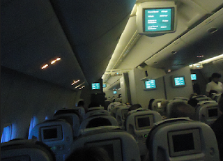 vista interna do avião com telas de entretenimento no corredor e poltronas