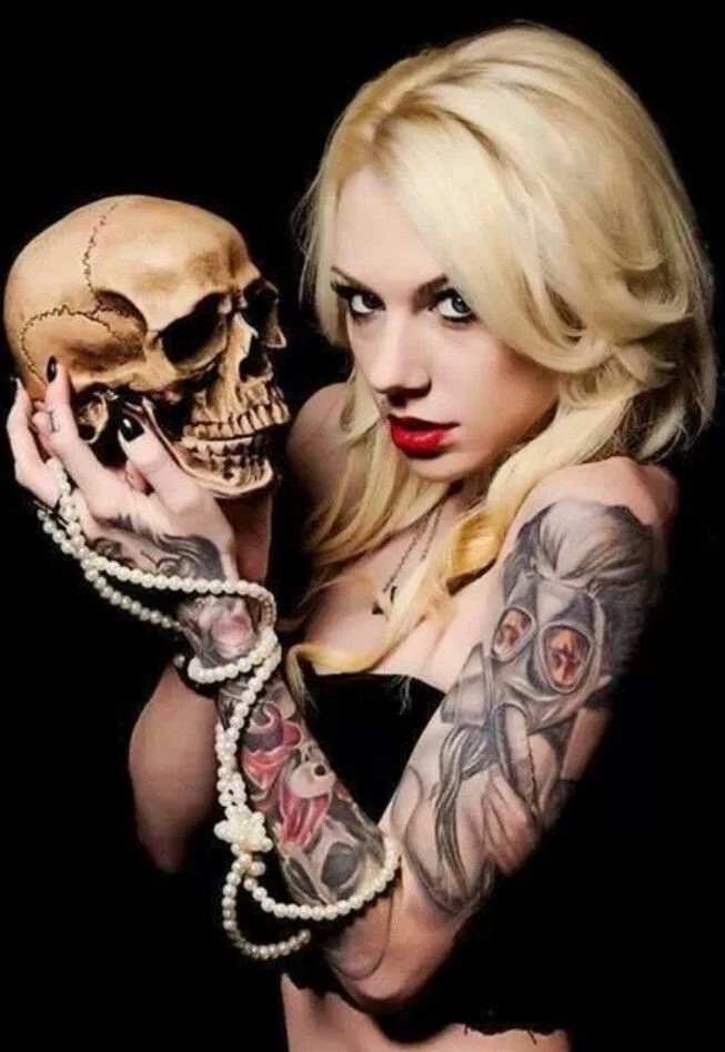 Espectacular mujer rubia sosteniendo una calavera, lleva tatuajes de craneos en el brazo