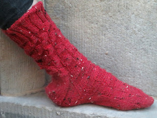 a red sock knit in fingering-weight yarn. The sock is worked in a knit and purl checkerboard pattern.