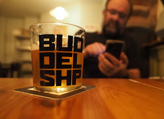Blurred man on phone in background, foreground a glass of beer
