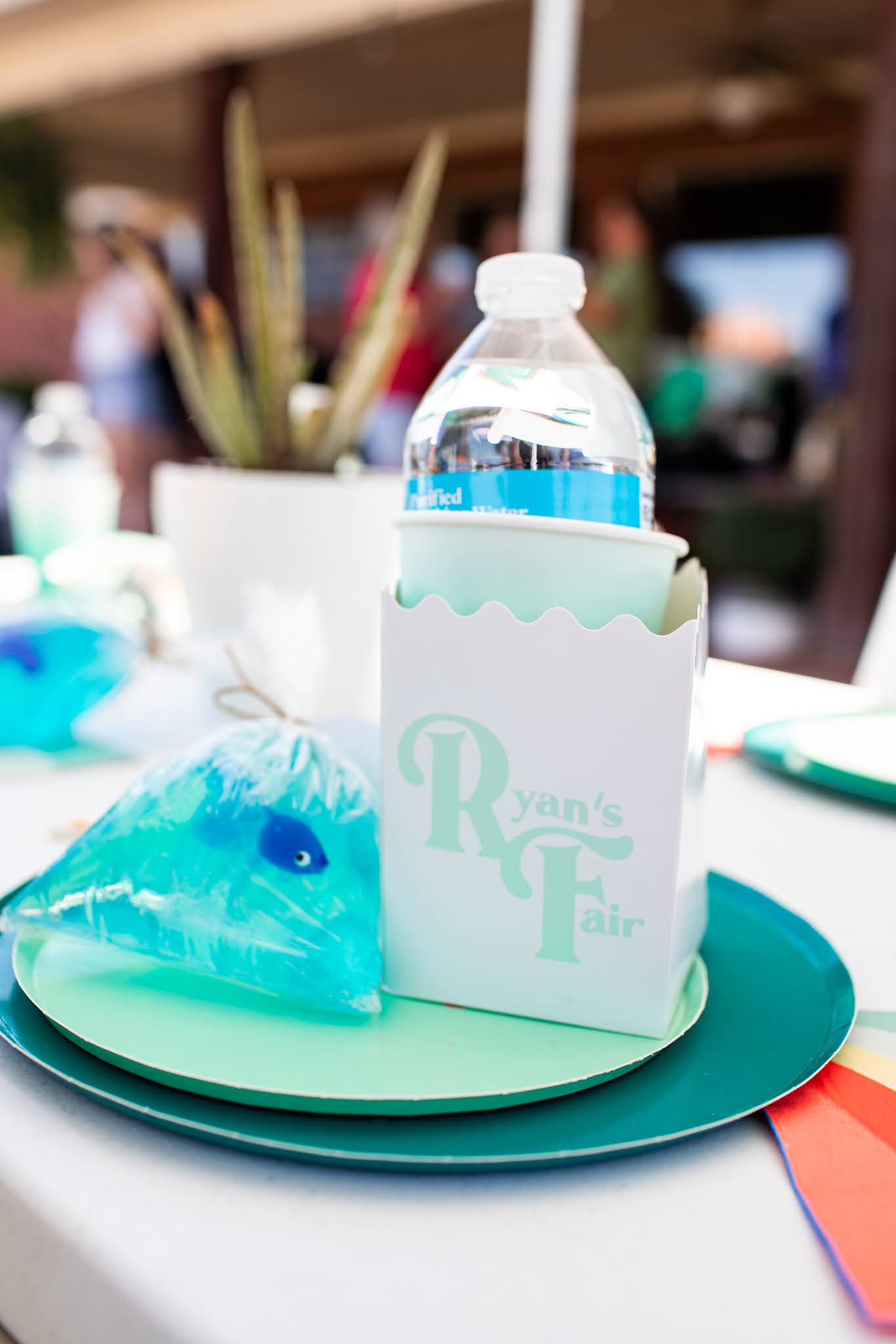 Table decor details with custom logo for fair themed birthday party with colorful napkins and fish in a bag soap favors