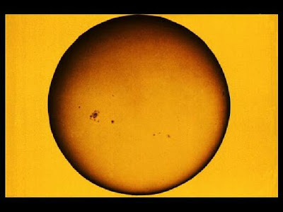   O Sol é a estrela mais próxima de nós. Todos os planetas do sistema solar giram ao seu redor e cada um com um período diferente. Ele é o responsável pelo suprimento de energia da maioria dos planetas. Quando as pessoas visitam observatórios as perguntas mais comuns que surgem a respeito do Sol são: o que é o Sol e como ele funciona? Do que ele é feito? Mas, antes de responder a essas perguntas veremos alguns dados curiosos a respeito do Sol.  O Sol só é uma estrela por causa da grande quantidade de massa que ele tem, 332 959 vezes a massa da Terra. Ele é constituído, principalmente dos gases hidrogênio e hélio, os dois gases mais leves que temos. Quando se diz que o Sol tem quase 98% de gases a pergunta mais comum que aparece é: como é possível o Sol ter tanta massa, ser tão grande sendo formado de gases?  Bem, essa é uma longa história e que nem mesmo os cientistas que estudam o Sol e outras estrelas sabem explicar exatamente como acontece, mas uma coisa eles sabem: Antes de existir o Sol e os planetas o que existia no lugar do sistema solar era uma enorme nuvem de gases e poeira muito maior que o sistema solar. Os gases são os que conhecemos: oxigênio, nitrogênio e principalmente hidrogênio e hélio; a poeira são todos os outros elementos químicos; ferro, ouro, urânio, etc... mas, a grande parte dessa nuvem era o hidrogênio e o hélio. Por algum motivo que ainda não é bem explicado essa nuvem encontrou condições para se aglomerar, se juntar em pequenos blocos, esses blocos começaram a se juntar em blocos cada vez maiores. Um desses blocos, o que se formou primeiro, no centro da nuvem, ficou tão grande e pesado que sua força gravitacional tornou-se suficiente para reter os gases com muita facilidade. Esse bloco aumentou tanto de tamanho e massa que acabou por se transformar numa estrela: o Sol. Os blocos menores que se formaram ao redor do bloco central deram origem aos planetas. CUIDADO! Muitas pessoas pensam que os planetas são pequenas bolhas expelidas pelo Sol. Isso porque os cientistas do século passado e começo deste século pensavam assim. Hoje em dia sabe-se que isso não é verdade. A teoria da nuvem de gás e poeira é a mais aceita entre cientistas atuais  LOCALIZAÇÃO  O Sol ocupa uma posição periférica na nossa Galáxia,ou seja, ele está a 33.000 anos luz do centro galáctico, o que corresponde a 2/3 do raio galáctico. Nós estamos num dos braços espirais, o braço de Orion, como mostra o esquema a seguir.   Figura 1: Localização do Sol na Galáxia  O Sol também está orbitando em relação ao centro gravitacional da nossa Galáxia. O ano do Sol é de aproximadamente 230 milhões de anos terrestres e sua velocidade orbital é de 250 km/s, sendo que todos os demais corpos do Sistema Solar o acompanham nessa viagem. Sabe-se que o Sol realizou cerca de 250 revoluções completas até hoje. A idade do Sol é de cerca de 4,5 bilhões de anos.    O Sol, estrela de quinta grandeza[1], é o principal componente do nosso Sistema Solar e o mesmo é um dos milhões de Sóis existentes em nossa Galáxia.  Se o Sol for colocado a distância de 32,6 anos-luz de nós, o seu brilho será semelhante ao de uma estrela de quinta magnitude. Objetos vistos ou comparados a essa distância, nós definimos o seu brilho como Magnitude Absoluta. O Sol tem magnitude absoluta igual a cinco, dai a expressão estrela de quinta grandeza.  CARACTERÍSTICAS GERAIS  Pela Lei da Gravitação Universal de Isaac Newton (1642-1727), foi possível obter a massa da nossa estrela que é estimada em 332 959 vezes a massa da Terra, equivalendo a 1,989 1030 kg, com um raio de 695 500 km . Sua densidade média é 1.4 g/cm3, mas a matéria não é homogênea em seu interior. A densidade no centro do Sol é muito maior, enquanto que nas camadas externas é muito inferior. O seu eixo de rotação tem uma inclinação em relação ao plano da eclíptica de 7° 15''.  Apesar de sua massa ser milhares de vezes maior que a da Terra, sua gravidade na superfície é apenas 28 vezes maior que a gravidade terrestre. A temperatura na sua superfície é de cerca de 5770 K, e não é uma superfície sólida, mas sim em estado de plasma e gás.  O fato de o Sol ser basicamente um corpo constituído por um fluido (plasma e gás), provoca o fenômeno conhecido como rotação diferenciada. A velocidade dessa rotação varia nas diferentes latitudes com um valor máximo no equador (2 km/s) correspondendo a 25,03 dias e uma mínima nos pólos com um período de 30 dias. Essas informações só foram possíveis graças às manchas solares, as quais nós abordaremos melhor mais adiante. Isso é a chamada rotação diferenciada, a qual nós representamos com o seguinte esquema.  Figura 2: Esquema da Rotação Diferenciada  O Sol representa 99,867% de toda a massa do Sistema Solar e a restante está dividida entre os planetas, asteroides, satélites, e cometas do Sistema Solar. A massa do Sol apresenta a seguinte distribuição:   Camadas Externas (Fotosfera e pouco abaixo) 0,2% de elementos pesados  7,8% de hélio  92% de hidrogênio  Tabela 1: Características Químicas.  Raio  695 500 km,  109 raios terrestres  Superfície  6,16 1013km2 11.881 vezes a terrestre  Volume  1,44 1018 km3 1,3 106 vezes o terrestre  Massa  1,9 1030 kg  334.672 vezes a terrestre  Densidade  1,4 g/cm3 0,26 vezes a terrestre  Luminosidade  3,9 1027 kW  --------- Temperatura Superficial  5770 K --------- Temperatura no Centro  1,5 107K --------- Gravidade Superficial  276 m/s2 28 vezes a terrestre  Tabela 2: Características Físicas do Sol.  O funcionamento do Sol e a sua Estrutura Interna  Quando só se conheciam as reações químicas (combustão) para a produção de fogo e calor, pensava-se que o Sol funcionava da mesma maneira, mas quando os astrônomos conseguiram calcular sua massa e quantidade de energia necessária para mantê-lo aquecido constatou-se que ele não iria durar mais de 100 anos. Como o Sol é muito mais velho que 100 anos, a natureza deveria ter criado outra maneira muito mais eficiente de se produzir energia. Só na primeira metade desse século é que se descobriu a existência da energia nuclear.  NÚCLEO: No Sol, a energia nuclear é produzida com o hidrogênio fazendo o papel de combustível. Sabendo como fazer a temperatura de um gás subir é possível entender como ocorrem as reações nucleares do Sol. Sabemos que, quando um gás é comprimido (pressionado) ele aquece. Perceber isso é fácil: encha um pneu de bicicleta usando uma bomba manual. O bico do pneu e a parte da bomba que está próxima do bico ficam bem aquecidos. Isso acontece porque o ar (gás) que está dentro da bomba é comprimido pela força que você faz. Quando o pneu fica quase cheio e você tem que fazer mais força, ou seja, comprime mais ainda o ar ele fica cada vez mais quente. Agora imagine no Sol onde a pressão é milhões de vezes maior que a pressão na Terra. Sabemos também que a pressão aumenta com a profundidade. Mergulhando numa piscina com 2 ou 3 metros já percebemos o aumento da pressão em nossos ouvidos. No Sol, pode-se afundar até 50 vezes o diâmetro da Terra sem chegar ao seu centro, fica até difícil de imaginar a pressão que existe lá. Toda essa pressão faz com que o hidrogênio atinja temperaturas de 15 milhões de graus no centro do Sol. Com o gás nessa temperatura e pressão é que ocorrem as reações nucleares que mantém o Sol aquecido. Essas reações são milhões de vezes mais poderosas que as reações nucleares produzidas na Terra. Além disso, não se conseguiu produzir, na Terra, reações do mesmo tipo que acontecem no Sol.   As reações nucleares do Sol transformam o hidrogênio em hélio e nessa transformação é liberada uma enorme quantidade de energia. Nós aqui na Terra recebemos uma pequenina parte da energia que o Sol produz.   Somente no século XX é que se atingiu conhecimentos teóricos suficientes para elaborar uma teoria a respeito de toda a energia que o Sol irradia . Sabe-se que o Sol está atualmente em equilíbrio térmico (temperatura média aproximadamente constante), mas nós sabemos também que ele emite muita energia na forma de calor e luz. Porém para se manter esse equilíbrio é necessário uma fonte interna de energia. Essa fonte está no seu núcleo, que através de reações termonucleares funde átomos de hidrogênio e forma átomos de hélio. Seu núcleo está a uma temperatura de 15 milhões de Kelvin e possui uma pressão da ordem de bilhões de atmosferas, sendo que esses valores vão decrescendo juntamente com a densidade, de modo não linear, conforme afasta-se do núcleo em direção à superfície. A variação térmica (considerada do núcleo para as camadas mais externas) determina a estrutura interna da estrela conforme o modo de propagação da energia. Os principais mecanismos de transporte energético encontrados no Sol são o radiativo e o convectivo, esquematizados a seguir:  O RADIATIVO: representado pela "Zona de Radiação'', é a camada do Sol onde a energia propaga-se da mesma maneira que a luz, ou seja, através da radiação e por isso não depende do meio para se propagar. O meio atua no sentido de atenuar a energia.  O CONVECTIVO: representado pela "Zona de Convecção'', é a camada do Sol onde a energia se propaga através de movimentos convectivos, ou seja, a parte que está em contato com a "Zona de Radiação'' é aquecida e, com isso, sua densidade diminui e tende a subir para a superfície e o que está na superfície desce para entrar em contato com a "Zona de Irradiação''. Esse é o mesmo processo que ocorre com a água fervente num recipiente em aquecimento no seu fundo.  Utilizando-se desse processo, o Sol está emitindo energia desde sua ignição a 4,5 bilhões de anos e os cálculos realizados indicam que ele emitirá energia da mesma forma por pelo menos mais 5 bilhões de anos, que é quando estarão esgotadas as reservas de hidrogênio em seu núcleo. É importante saber que a emissão de energia do Sol não é uniforme, ou seja, há variações no fluxo de energia emitida, que pode chegar, em casos excepcionais, a 5% do fluxo médio de energia. Atribuindo-se o nome de "Sol calmo'' quando ele mantem-se no mínimo de emissão de energia e "Sol ativo'' quando está no máximo de emissão. Esse mínimo ou máximo é observado quando há um número menor ou maior de fenômenos em todas as suas camadas. Essas variações influenciam o meio interplanetário, sendo que na Terra observa-se muitos efeitos na atmosfera e no campo magnético.  Figura 3: Esquema da Estrutura do Sol    Figura 4: O Sol visto no Visível com um filtro neutro  CAMPOS MAGNÉTICOS  George Ellery Hale (1868-1938) foi quem detectou os campos magnéticos solares. Utilizando-se de um instrumento, o espectrógrafo de alta dispersão, ele descobriu que algumas linhas produzidas nas proximidades das manchas solares eram duplas e até mesmo triplas ou seja, no lugar de uma linha com certo comprimento de onda, via-se uma linha à direita e à esquerda daquele comprimento de onda e até mesmo a original e duas outras laterais. Esse fenômeno de duplicação de linhas é chamado de efeito Zeeman e ocorre quando a fonte emissora de luz está submetida a um campo magnético (nesse caso a fonte emissora é a mancha solar). Hale pôde calcular o campo nessa região que chega a 5000 Gauss e ainda conseguiu provar que o campo magnético geral, gerado pelo Sol, é da ordem de 1 a 2 Gauss. Esse campo magnético está dirigido de norte para sul, porém nas regiões onde se encontram os campos magnéticos intensos (1000 Gauss), estes estão dispostos, no sentido leste-oeste. O estado de plasma, que se encontra a matéria Solar, oferece pouca resistência à corrente elétrica o que faz com que toda a estrela se comporte como uma bobina elétrica.  Descobriu-se posteriormente que as linhas de força do campo magnético estão confinadas no plasma, ou seja,   comportam-se como se estivessem ligadas às particulas que o compõem e acompanham o fluxo de matéria. Com isso a rotação diferenciada acaba deformando essas linhas como se fossem tiras de borracha. As linhas do campo magnético sofrem um processo de condensação, até cada grupo assumir a forma espiralada. Daí encontram-se espirais ao longo de todos os meridianos e todas no sentido leste-oeste (sentido de rotação). A concentração dessas linhas equivale a maior intensidade dos campos magnéticos em relação a situação inicial, e como a rotação não é uniforme cada espiral pode ser esticada até formar um laço. Em certos momentos os laços se rompem e afloram na superfície. Nesse momento temos a formação das manchas solares.  ESTRUTURA EXTERNA DO SOL  FOTOSFERA: Aparentemente a olho nu e com instrumentos de baixa precisão a superfície solar é bastante uniforme. Na realidade ela é formada por pequenas estruturas hexagonais, os grânulos, de forma irregular e separadas por zonas mais escuras. Verificou-se posteriormente que essas estruturas são topos de colunas ascendentes de gás aquecido que ao se resfriarem descem pelas zonas escuras vizinhas decorrentes dos processos de convecção, que mistura o gás nas camadas inferiores à fotosfera. Estima-se que a diferença de temperatura entre os grânulos e as zonas escuras é de cerca de 1000 K.   Como o campo magnético é muito intenso em certas regiões (pelos efeitos explicados anteriormente) as linhas ficam quase perpendiculares à superficie e a matéria tende a se mover ao longo das linhas, nesse caso, a matéria fica "confinada'' a elas. Com isso há um bloqueio no movimento convectivo e o plasma desloca-se verticalmente, acompanhando as linhas e não horizontalmente para descer pelas zonas escuras. Então reduz-se a propagação do calor em certas áreas, que se tornam mais frias que as áreas circunvizinhas, emitindo pouca radiação. Isto é que caracteriza a mancha solar na fotosfera.  Constatou-se que o número de manchas solares sofre variações periódicas e essas variações estão ligadas ao "Sol calmo'' e ao "Sol ativo''. Partindo do "Sol calmo'' ,estágio de mínima atividade, observa-se que durante 4,6 anos há um aumento rápido das manchas atingindo um valor máximo. Após esse máximo transcorrem cerca de 6,4 anos onde se constata uma diminuição gradual nas manchas, atingindo novamente uma atividade mínima. No total entre um estágio de 4,6 anos de "Sol ativo'' e o outro estágio de 6,4 anos de "Sol calmo'' decorrem cerca de onze anos. Embora cada onze anos de atividade seja igual ao outro no seu aspecto visual, deve-se considerar que a polaridade magnética do Sol se inverte, ou seja, as  manchas que ocorreram no hemisfério norte durante o "Sol ativo'', irão ocorrer no hemisfério sul no estágio correspondente ("Sol ativo'') e vice-versa. Com isso nós temos um período completo vinte e dois anos de atividades solares, quando então o ciclo recomeça.  CROMOSFERA: É uma região externa à fotosfera. A temperatura na cromosfera se reduz a partir da fotosfera até atingir 500 km de altitude com 4000 K e, então há novamente um aumento até atingir 9000 K a altitude de 2000 km quando se inicia a coroa. A observação da cromosfera, por muito tempo só foi possível quando ocorriam eclipses totais que encobriam a luz fotosférica. Só há poucas décadas desenvolveu-se um instrumento , o coronógrafo, que simula o eclipse solar total, e nada mais é do que um telescópio preparado com filtros e obstáculos especiais que permitem somente a passagem da luz da cromosfera e coroa.  Ocorrem ainda as protuberâncias solares que se elevam da cromosfera para a coroa. Estas são visíveis sem instrumentos durante os eclipses solares totais, ou com o auxílio do coronógrafo. Essas protuberâncias podem ser eruptivas, de rápida duração, ou protuberâncias quiescentes que podem durar várias rotações solares. As protuberâncias possuem uma densidade muito superior à coroa circundante e temperatura de 10.000 a 20.000 K. Esses fenômenos são devido à assossiação de campos magnéticos que variam de 20 a 200 Gauss.  Quando as explosões que dão origem às protuberâncias ocorrem, e isso aparece principalmente nas proximidades das manchas solares na fotosfera, é que se percebe a influência do Sol sobre a atmosfera terrestre. Tal atividade pode interromper as comunicações a longa distâncias. Ocorre que partículas com muita energia são lançadas ao espaço e atingem a Terra provocando uma ionização da atmosfera terrestre. Em consequência, a ionosfera (camada atmosférica terrestre) deixa de refletir as ondas de rádio emitidas pelo Sol para o espaço e as ondas de rádio das emissoras de volta para a Terra, podendo interromper as comunicações a longa distância. Grande parte da radiação emitida pelo Sol atenua-se na nossa atmosfera, a qual atua como filtro bloqueando as radiações mais prejudiciais às formas de vida na superfície terrestre.  COROA: É a camada mais impressionante do Sol e a mais extensa delas (abrange praticamente todo o Sistema Solar). A densidade da matéria nessa camada é cerca de 10 milhões de vezes menor que na fotosfera e diminui conforme se afasta do Sol. Em condições normais também não pode ser vista, pois a sua emissão de luz é um milhão de vezes menor que a luz da fotosfera. Pode ser visualizada em eclipses solares totais e com o coronógrafo. A Coroa pode ser distinguida em três regiões: Coroa interna com expessura 1,3 raios solares a partir da cromosfera; Coroa intermediária que vai de 1,3 a 2,5 raios solares e a Coroa externa de 2,5 a 24 raios solares. Ao longo da translação terrestre, a Terra caminha imersa na coroa solar, e a radiação presente nela (advinda do Sol) bombardeia continuamente nosso planeta.   Figura 5: O Sol observado através do ultravioleta evidenciando uma protuberância. Para podermos imaginar o quanto essa reação nuclear é poderosa vamos fazer a seguinte comparação. Se o Sol fosse formado pelo combustível mais eficiente que se conhece, que é o combustível usado no ônibus espacial, e todo o Sol fosse queimado, ele duraria cerca de 100 anos. Sendo movido a energia nuclear apenas 1/3 do hidrogênio do Sol será consumido e mesmo assim os cientistas acreditam que ele irá funcionar por mais 5 bilhões de anos. Considerando que ele já tem quase 5 bilhões de anos, a vida do Sol será de aproximadamente 10 bilhões de anos, ou seja o Sol irá durar 100 milhões de vezes mais do que se fosse movido por energia química.