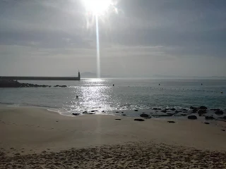 Beach, sea on the left side a wall of a habour