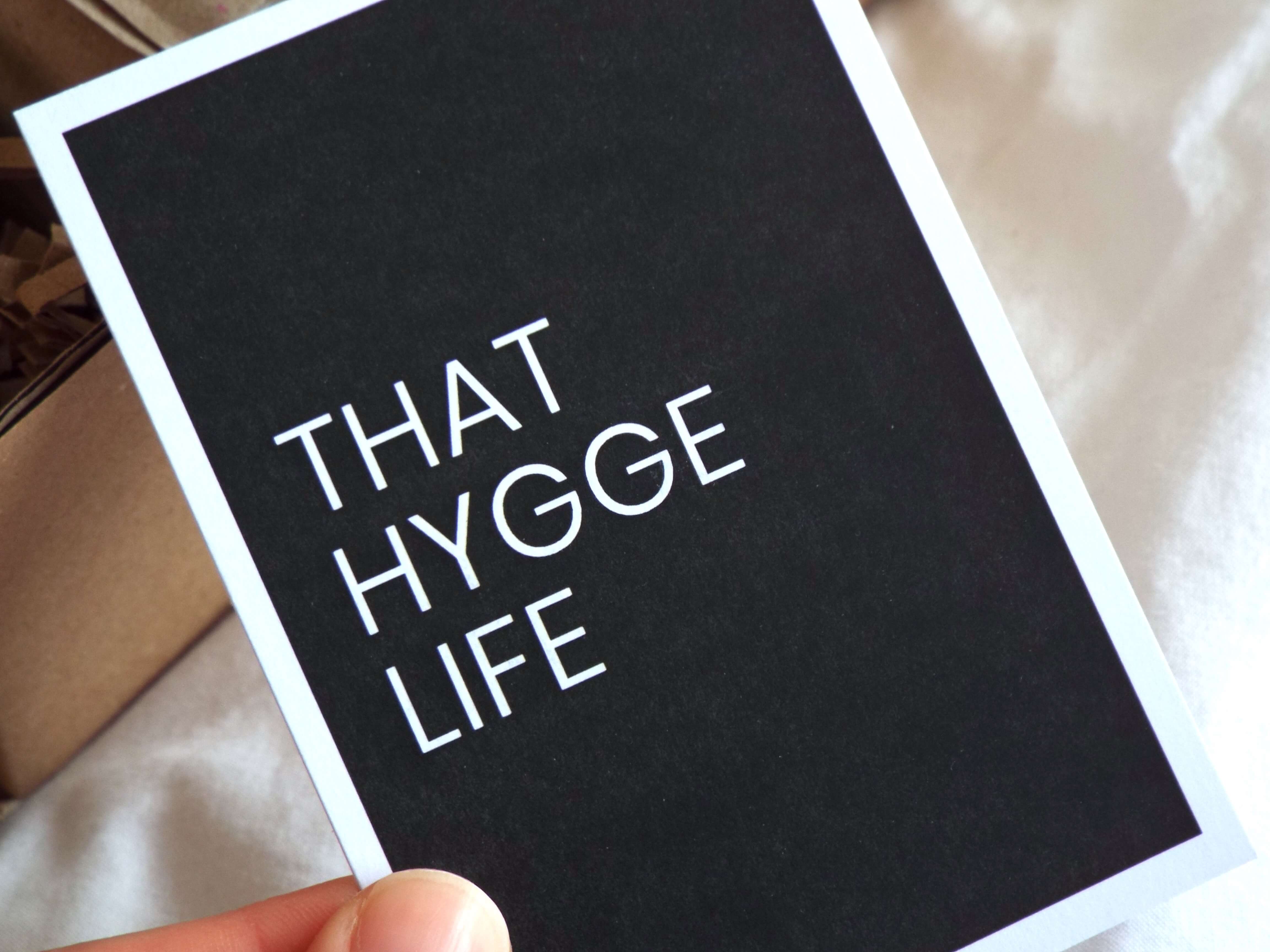 That Hygge Life black and white quote card held between two finger, close up shot.