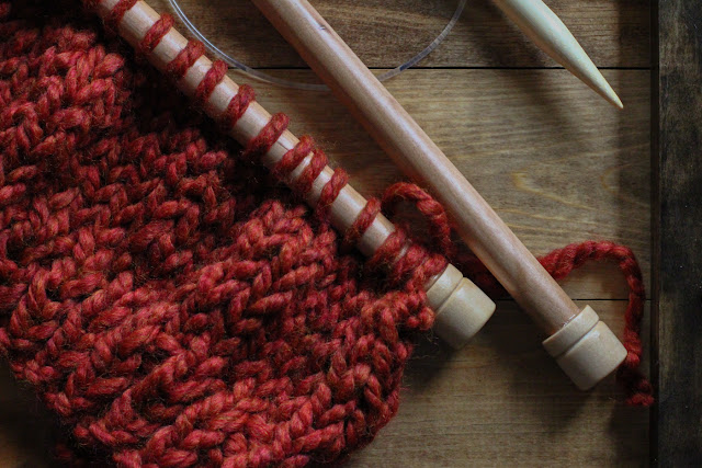 Chunky rusty yarn on large straight bamboo knitting needles on a wooden tray