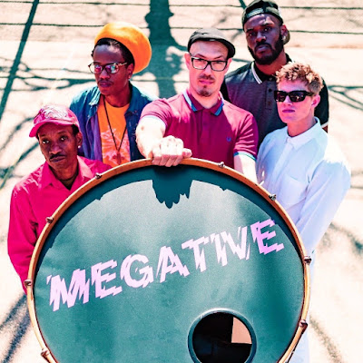 The band poses in back of a drum head with Megative printed on it.