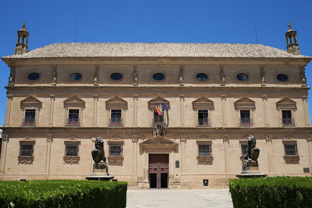 Fachada de palacio antigua con el cielo azul al fondo y jardines a su frente.